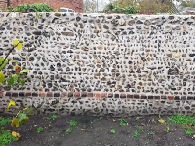 Repaired flint boundary wall with red brick banding.