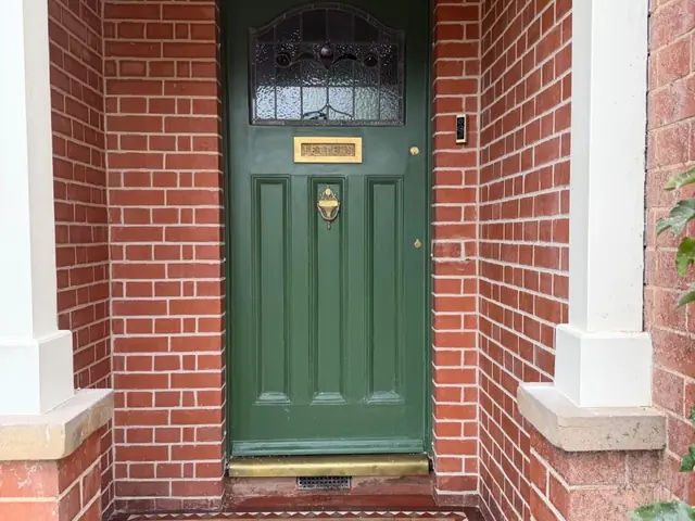 Restored brick entrance porch with a green front door and patterned tiled floor.