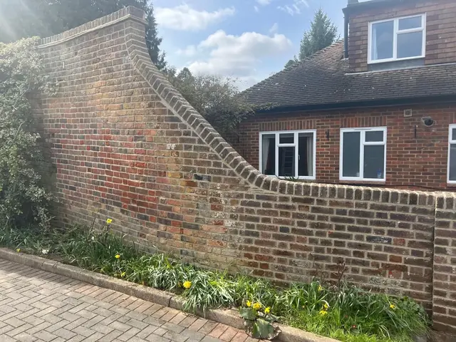 Curved red brick garden wall beside a paved driveway before repair.