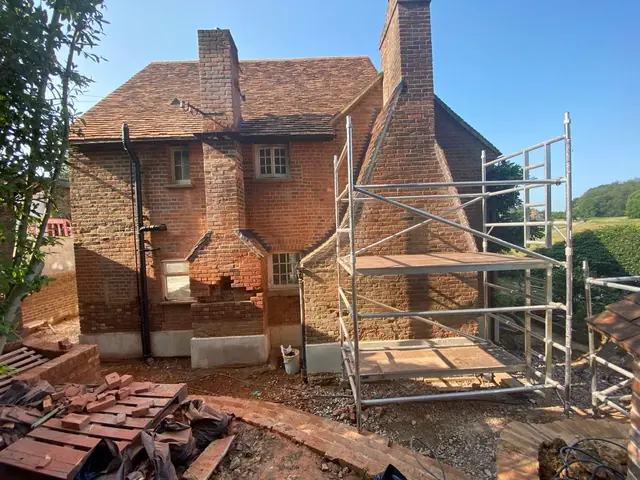 Rear elevation of a period brick house with scaffold and masonry work underway.