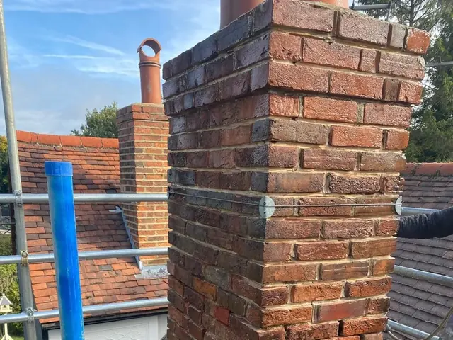 Brick chimney stack prepared for repointing on a scaffolded roof.