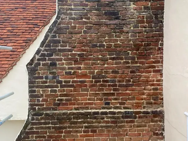 Weathered brick gable with dark staining and eroded joints before repointing.