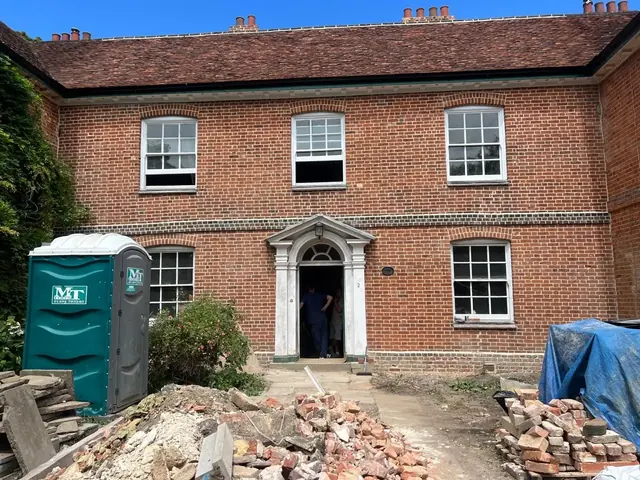 Long red brick period building with masonry work and rubble in the courtyard.