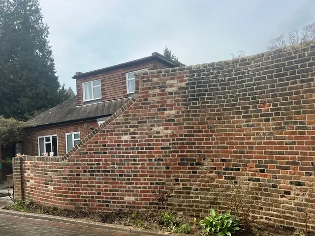 Tall curved brick garden wall showing weathered mortar before repair.