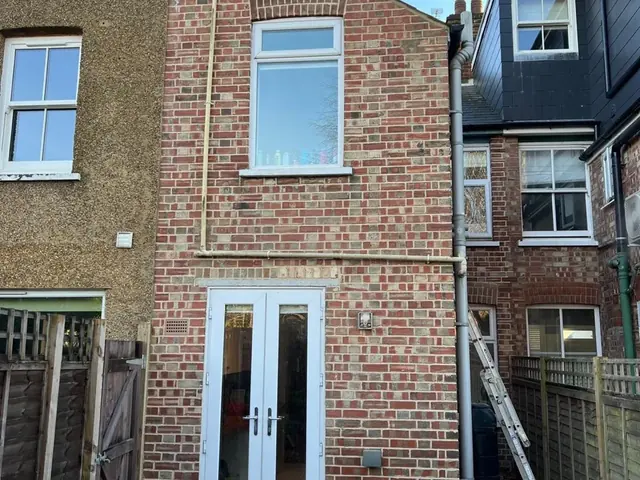 New red brick rear extension with white double doors and matching brickwork.