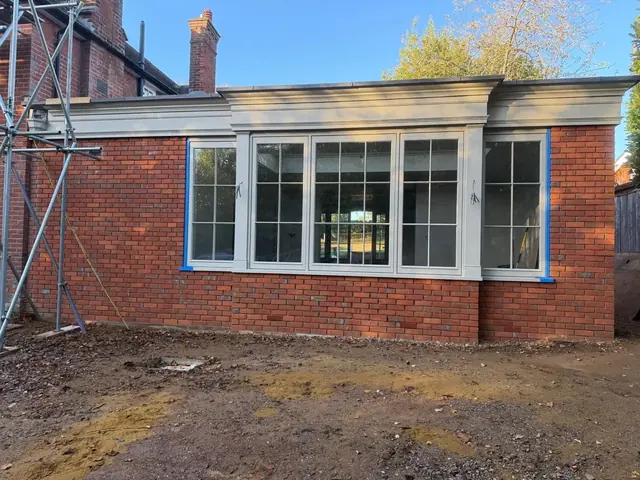 Completed red brick extension with large white timber windows and a decorative cornice.