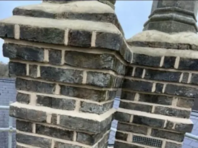 Twin chimney stacks with weathered brickwork viewed from roof scaffolding.