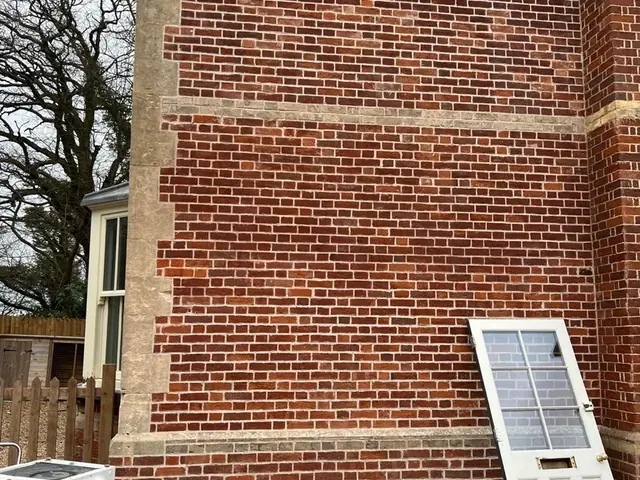 Large red brick gable wall after repointing, with pale stone bands.