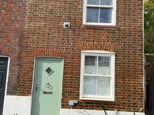 Small red brick cottage after repointing, with a pale green front door.