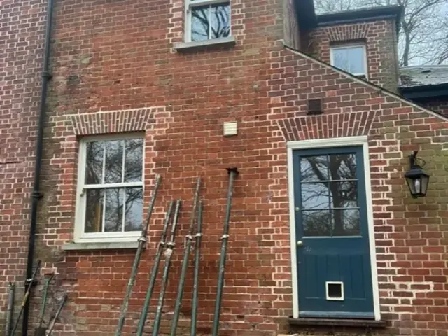 Rear elevation of a period lodge before restoration, with scaffold poles stacked outside.