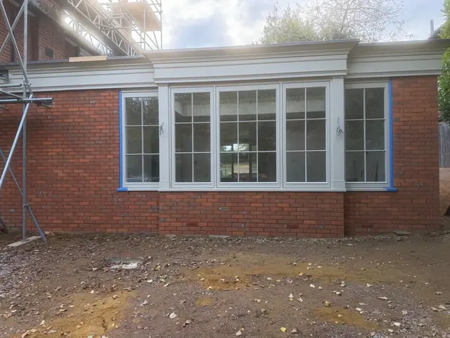 Red brick extension with large white windows during finishing work.