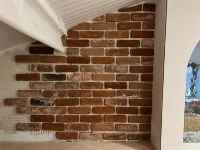 Exposed brick feature wall beneath a sloping ceiling during interior work.